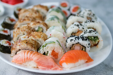 Sushi set on a large white oval plate. Soy sauce, pickled ginger and wasabi. Close-up. Soft focus.