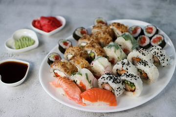 Sushi set on a large white oval plate. Soy sauce, pickled ginger and wasabi. Soft focus.