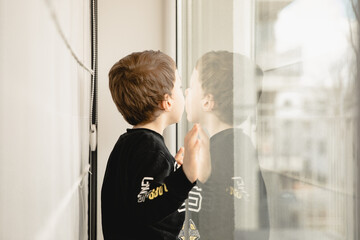 mały chłopiec stoi wewnątrz mieszkania i patrzy przez duże okno  
