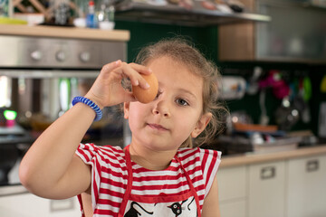 Bambina bionda in cucina pesa un uovo prende un uovo e lo porta vicino all'occhio