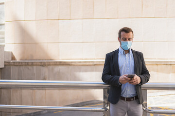 Man with a mask on his face and wearing a suit while is using a cell phone
