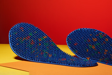 Blue massage insole for feet, with metal needles, spikes, on a yellow-orange background. For relaxation, health. Advertising, thematic and subject shooting. thorny subject