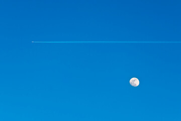 Jet trail and full moon on blue sky
