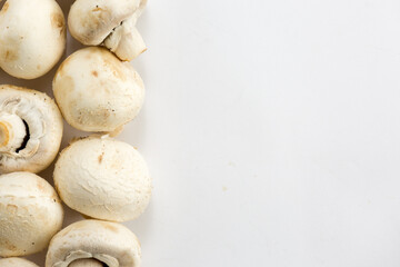 champignon mushrooms lie vertically on the left on a white background. The concept of minimalism in the kitchen. Place for text. Top view, flat lay, copy space right. Selective focus