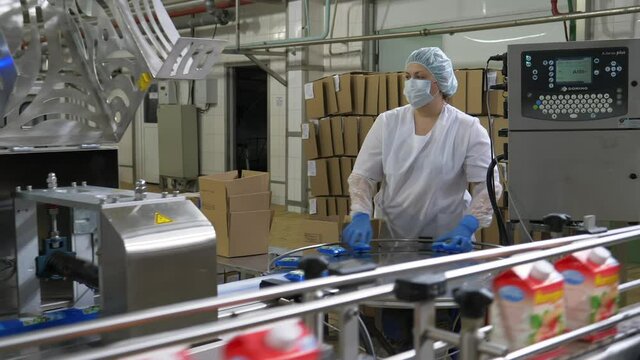 Seriouse female factory worker at routine work in dairy production plant, conveyor, prepared product in package
