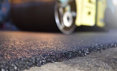 Road repair, thin layer of new asphalt close-up and road roller