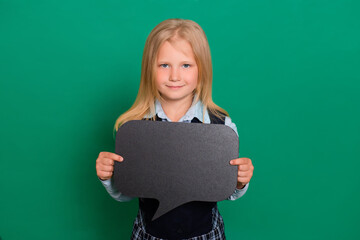 Little schoolgirl posing with a black board for inscriptions in hands isolated on a green background. Concept of idea, message.