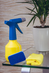 A detergent in a yellow blue cap bottle, a rag, bast lies on a glass table. flowerpot. Quarantined...