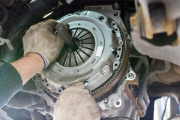 Car repair in a car service. Replacing the clutch disc of a gearbox on a car at a service station. Hands of a professional car mechanic. Cars repair technology. Technical photography. - obrazy, fototapety, plakaty