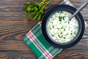Cold soup with fresh cucumbers, radishes with yogurt in a bowl on wooden background. Traditional Russian food - okroshka. Vegetarian food. View from above. Healthy food concept.
