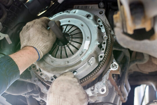 Car repair in a car service. Replacing the clutch disc of a gearbox on a car at a service station. Hands of a professional car mechanic. Cars repair technology. Technical photography.