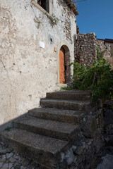 Fototapeta na wymiar A shaded, old, stone-clad concrete staircase following the path through an Italian village on a sunny day