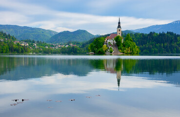 Beautiful morning at Lake Bled and Julian Alps in the background. The lake island and charming little church dedicated to the Assumption of Mary are famous tourist attraction in Slovenia