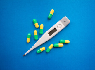Thermometer with medical capsules on a blue background