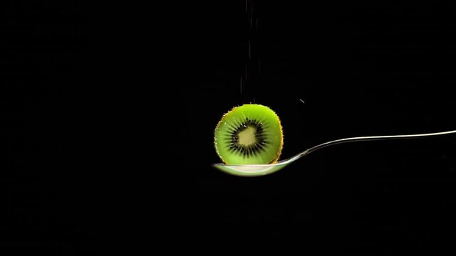 medio kiwi en fondo negro rociado de az&uacute;car blanca en c&aacute;mara lenta