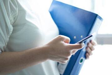 Frau hält blaue Datei, Stift und Handy in der Hand