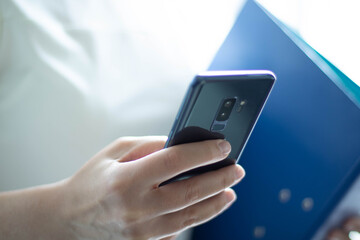 Frau hält blaue Datei, Stift und Handy in der Hand