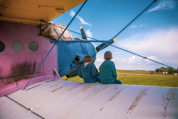 Two boys are sitting on the wing of the plane
