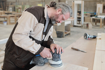 Mature worker of furniture producing factory smoothing surface of workpiece
