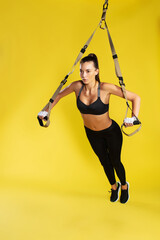 Working hard. Full length of young athletic woman in sportswear doing push ups with trx fitness...