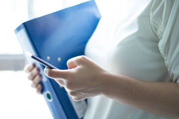 Frau h&auml;lt blaue Datei, Stift und Handy in der Hand