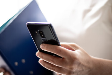 Frau hält blaue Datei, Stift und Handy in der Hand