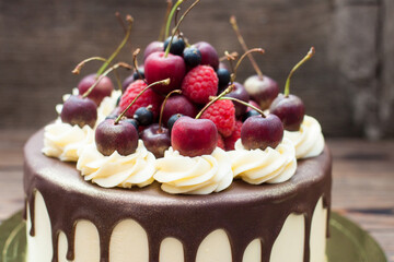 Birthday cake decorated with melted chocolate, whipped cream and fresh cherries. Rustic wooden background.
