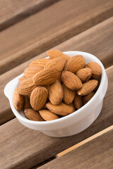 Almonds in white bowl on wooden background