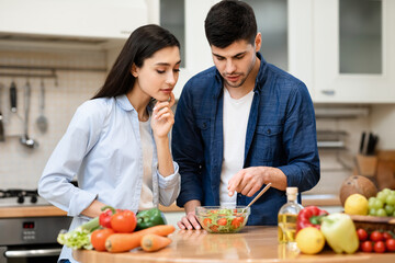 Young couple preparing salad together at their cozy apartment