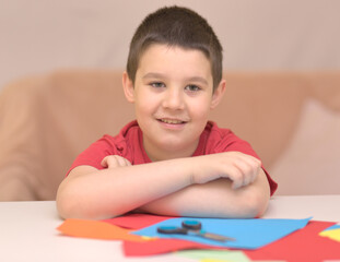 Cute smiling boy is cutting paper using scissors.  Education, school concept