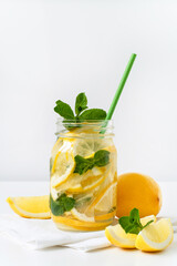 Refreshing summer drink. Lemonade in a glass jar with green paper straw, lemon slices and mint. Closeup.