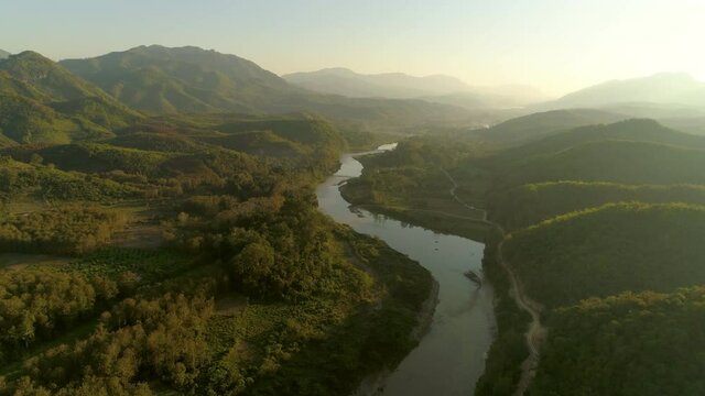 Aerial shot of river amidst green forest during sunrise, drone flying forward over landscape against sky - Tat Sae Waterfalls, Laos
