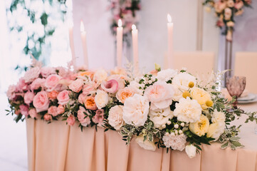 Banquet, restaurant. Table setting. On the table is a pink tablecloth. Presidium, table of the newlyweds. There is a tablecloth on the table. Floral arrangements in peach pink hues. Tall candles