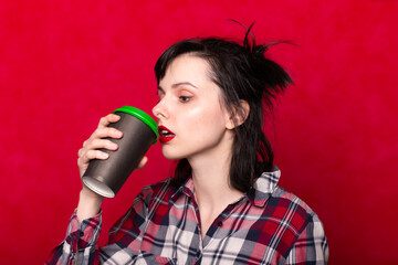 beautiful woman in red drinks coffee from a disposable cup, coffee to go, red background