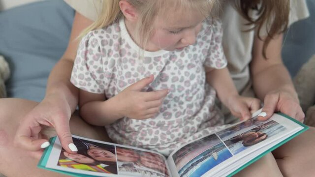 Mom shows little daughter family photos in a beautiful photo album.