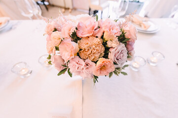 Peach pink floral arrangement. Banquet, restaurant. Table setting. White plates with a gold rim, golden cutlery, glasses. 