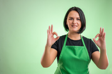 Female cook with green apron and black t-shirt showing double OK sign