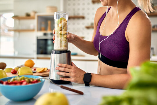 Unrecognizable sportswoman blending fruit and making smoothie in the kitchen.