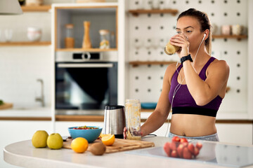 Young female athlete drinking fruit smoothie in the kitchen.