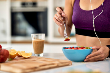 Close-up of athletic woman eating fruit salad in the kitchen.