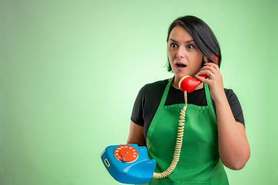 Female cook with green apron and black t-shirt looking surprised while talking on an old phone