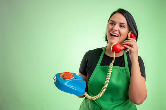 Female cook with green apron and black t-shirt laughing while talking on an old phone
