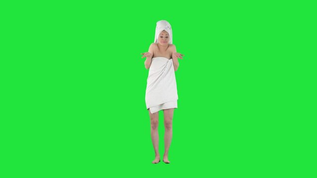 Young woman wrapped in towel after bath apologize and excusing after accidental mistake on solid green screen keyed background. 