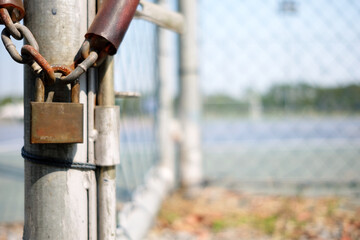 Old Rusty Padlock Hanging on Chain with Blurred Metal Fence Background.