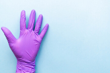 Hand of surgeon in violet medical glove showing five fingers gesture, isolated on a light blue background.