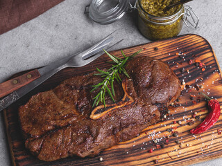 juicy grilled beef steak with bone on a cutting board,  spices, sauce pesto