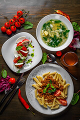 three-course set on a table. Tasty lunch set made of three meals, such as soup,  salad and pasta penne bolognese