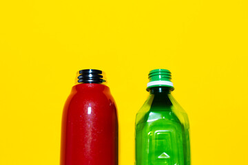 Close-up of two opened water bottles. Reusable steel thermo bottle of red color and disposable plastic bottle of green. Studio background of yellow.