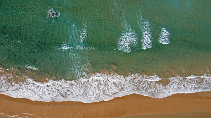 Vista cenital de olas rompiendo sobre la arena de una playa, agua cristalina, espuma de mar en la orilla