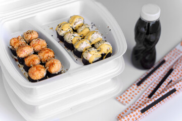 Hot baked rolls in a plastic box with soy sause and chopsticks (close up). Delivery service consept.